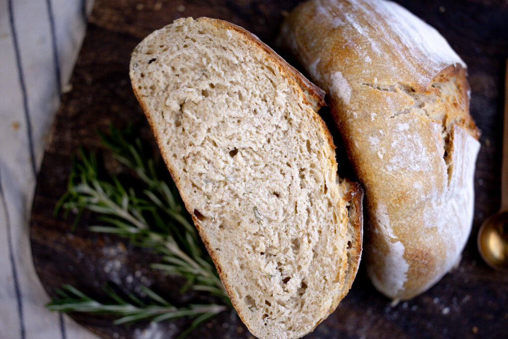 loaf sliced in half with rosemary beside it